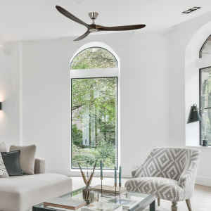 Luminaire et ventilateur intégré au plafond dans un salon lumineux avec canapé et fauteuil près d’une grande baie vitrée.